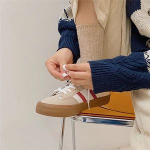 Close-up of beige canvas sneakers with red stripes and brown rubber soles during lacing