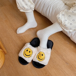 Close-up of cozy white plush slippers with yellow smiley faces on wooden floor