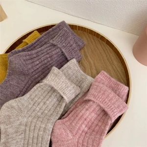 Flat lay of colorful thick wool socks in yellow, purple, and pink on a wooden tray