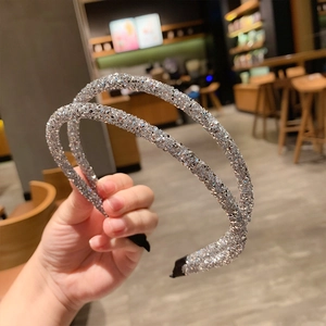 Close-up of two silver glitter headbands with black anti-slip tips held in a cafe setting
