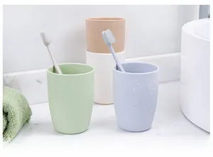 Close-up of matte plastic toothbrush cups in pastel colors with water droplets on marble