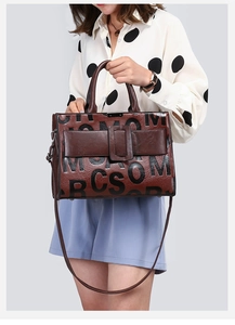 Reddish brown leather handbag with black letter patterns shown in a handheld lifestyle view