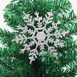 Close-up of a silver glitter snowflake ornament hanging on a green Christmas tree