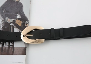 Detail of a chic black belt featuring a polished irregular gold buckle on a fashion magazine