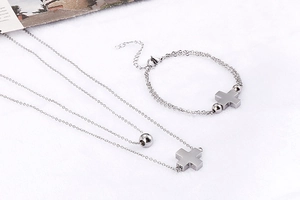 Flat lay of double-layer stainless steel cross necklace and bracelet set on white fabric