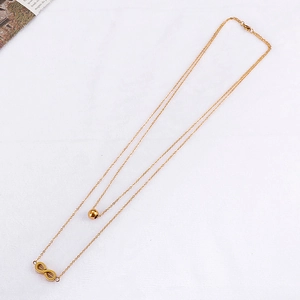 Double-layered gold necklace with infinity symbol and bead charm on white fabric
