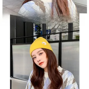 Detail of yellow knit beanie with daisy embroidery and gray argyle pattern sweater