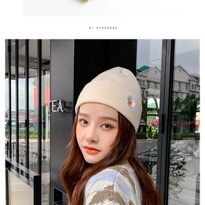 Close-up of beige knit beanie featuring delicate daisy embroidery worn by a model