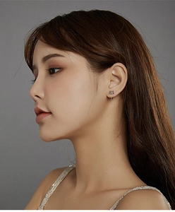 Close-up of model wearing small cat-shaped sterling silver stud earrings on grey background