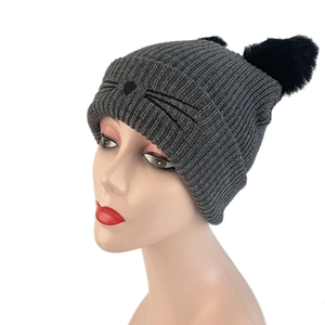Detail view of the cat ear knit hat showing plush poms and whiskers embroidery details