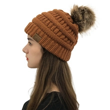 Close-up of caramel leopard knit beanie with brown fur pompom and C.C brand label