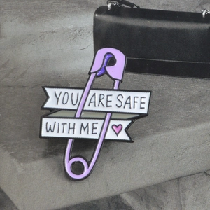 Purple enamel paperclip pin with You Are Safe With Me banner on a grey textured surface