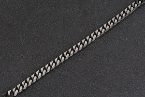 Vue macro d'une chaîne gourmette en métal gris fusil mat sur fond noir texturé