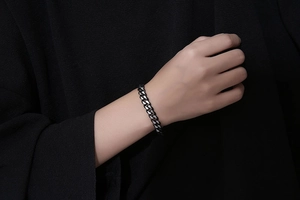 Détail d'un bracelet gourmette épais en métal gris foncé mat au poignet d'un mannequin