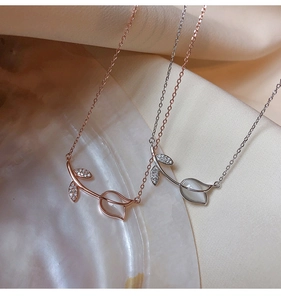 Detail of rose gold and silver leaf necklaces with cat eye stones on a seashell