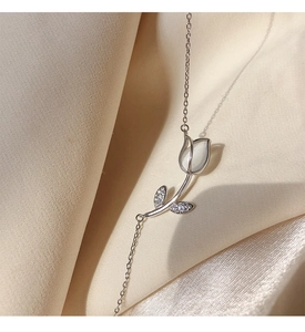 Macro shot of a silver tulip necklace with opal petals and zircon leaves on silk fabric
