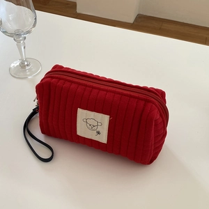 Dettaglio trousse in velluto a coste rosso con toppa a pecora e cinturino nero a mano