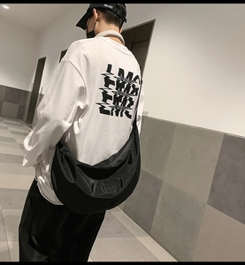 Street style view of a large black nylon crossbody bag worn by a person in a corridor