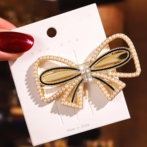 Detailed view of luxury bow-shaped hair clip with pearls, rhinestones and black enamel