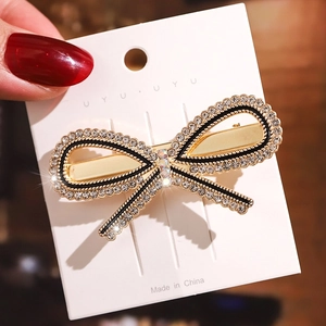 Close-up of a golden bow hair clip with white rhinestones on a white display card