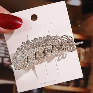 Detailed view of silver feather hair clip with sparkling rhinestones on display card