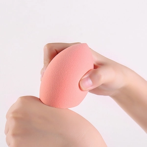 Vue détaillée d'une éponge de maquillage orange non latex tenue pour une application précise