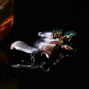 Macro shot of squirrel enamel brooch with silver fur on a branch against black mirror