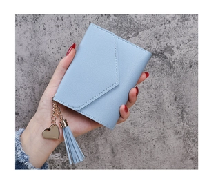 Close-up of light blue tassel wallet with heart pendant held by a hand in detail view
