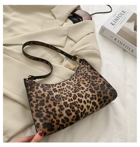 Detail of leopard print underarm bag with gold hardware on a beige blazer and magazine