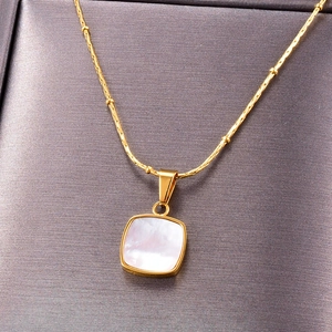 Gold stainless steel necklace with square white shell pendant on grey velvet background