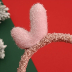 Close-up of pink plush antlers on a beige faux fur headband with Christmas festive background