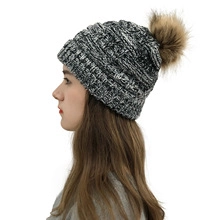 Detail of black and white knit beanie featuring a brown faux fur pom-pom on top