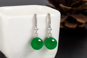 Detailed view of silver dangle earrings with green agate beads hanging on a white ceramic cup