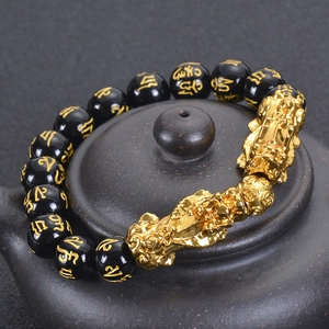 Detailed view of black obsidian beads with gold mantras and Pixiu charms on a tea lid