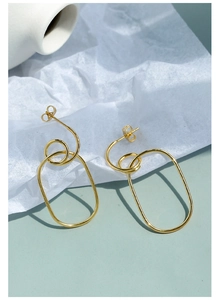 Macro shot of minimalist gold-plated geometric oval hoop earrings on textured paper