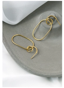 Detail showing oversized gold geometric hoop earrings on a luxury gray display tray