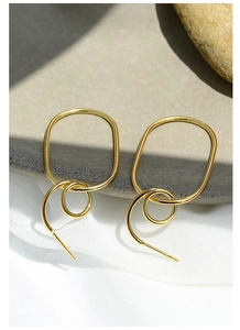 Detail of gold geometric earrings on grey stone and white fabric with sharp shadows