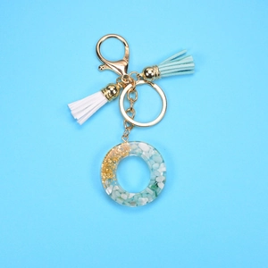 Detail view of resin letter O keychain with gold foil, green stones and dual tassels