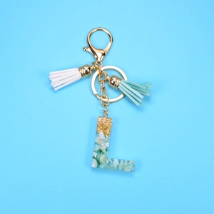 Detail of resin letter L keychain with gold foil, teal stones and soft tassels
