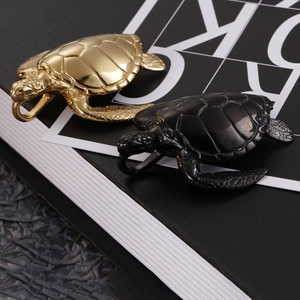 Detail view of turtle pendants in gold and black steel finishes on a book cover