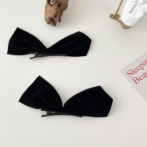 Detail view of two chic black velvet bow hair clips on a minimalist white table setting