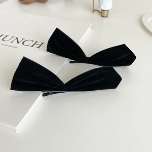 Close-up of a pair of black velvet bow hair clips with soft texture on a white desk