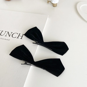 Detailed view of two black velvet bow hair clips on a minimalist white book background