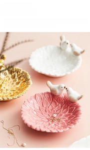 Macro detail of ceramic bird jewelry dish showing floral texture and metallic bird accent