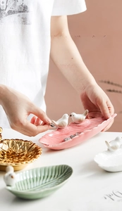 Detailed view of hand holding a leaf-shaped ceramic jewelry tray with a small bird figurine