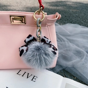Detailed close-up of grey fox fur pom pom keychain with leopard print bow and gold chain