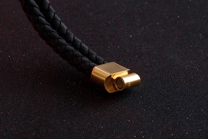 Macro shot of gold magnetic clasp and black braided leather strap on a cross bracelet