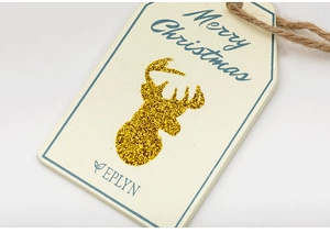 Close-up of wooden Christmas tag with golden glitter reindeer and rustic twine rope