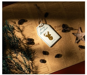 Close-up of Merry Christmas wooden tag with golden reindeer on vintage newspaper background