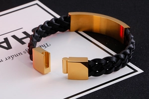 Detail of black braided leather bracelet with polished gold-plated metal plate and clasp
